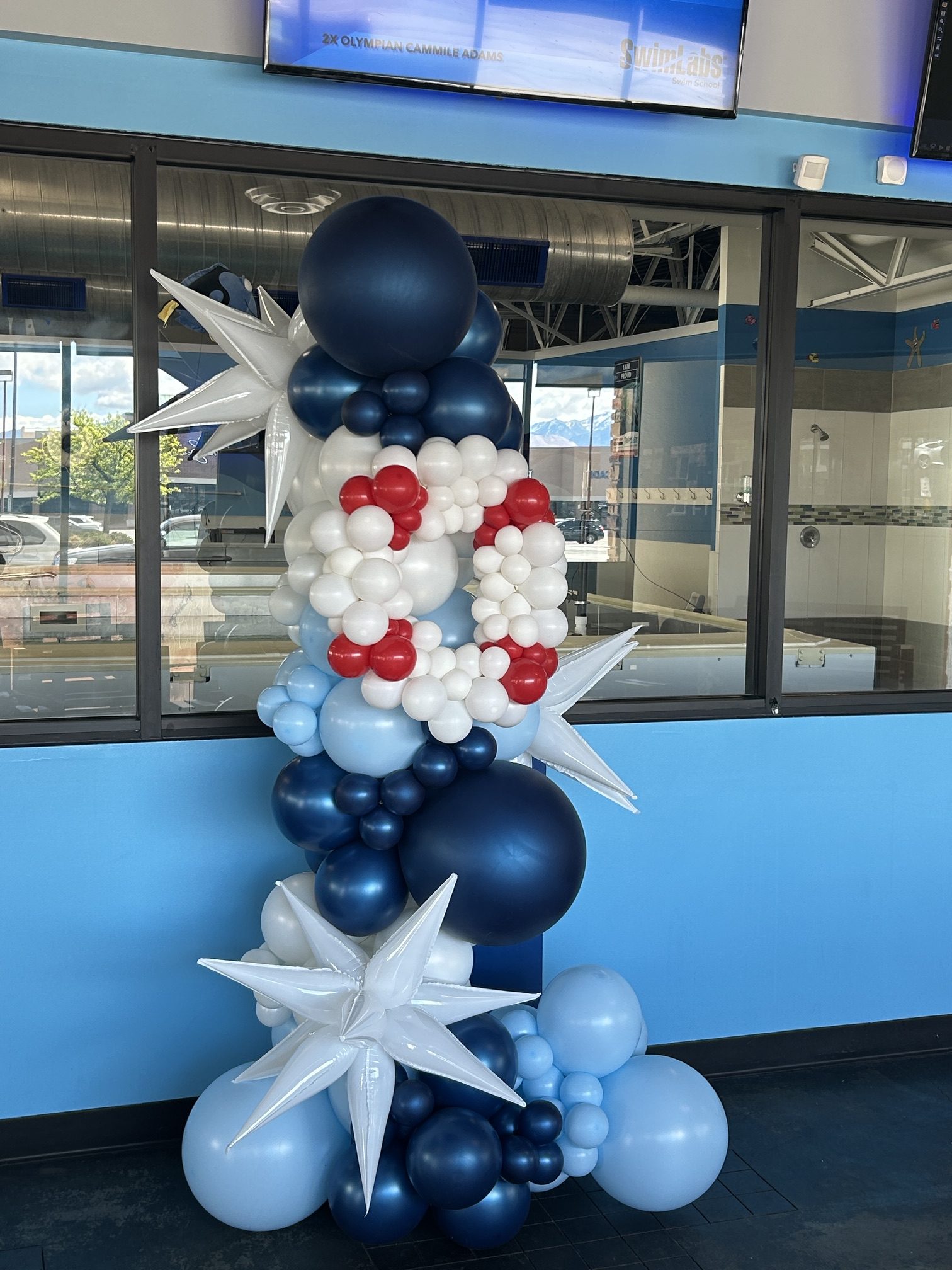 This 7‑foot vertical garland was created for SwimLabs using a crisp palette of navy, light blue, and white. The custom balloon life preserver adds a playful nod to their swim‑training brand — a perfect touch for a company co‑owned by three‑time Olympic gold medalist Rowdy Gaines. This install brings height, color, and personality to their space while keeping the look clean and professional.